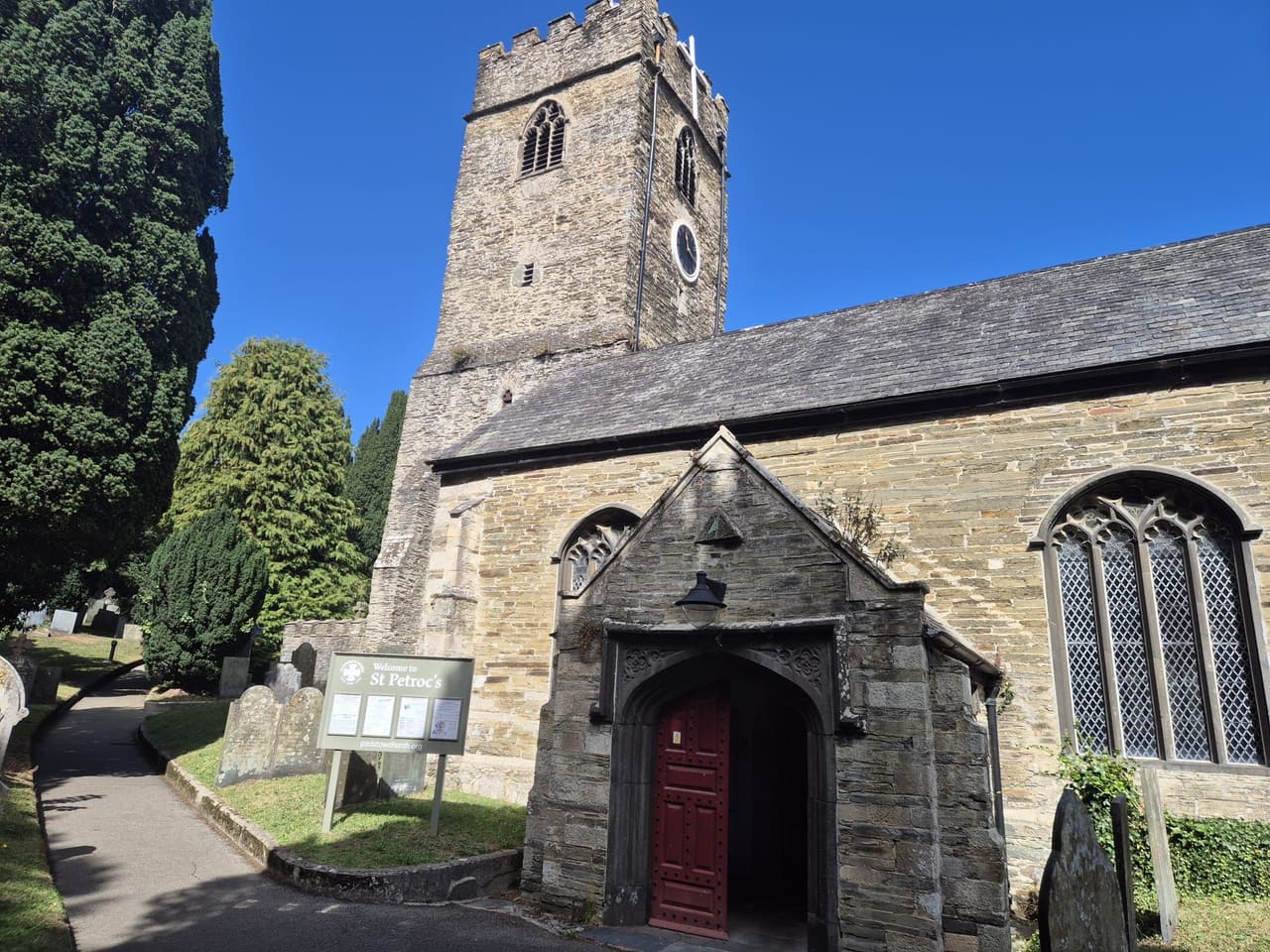 St Petroc's Church's crenellated tower and stone porch, seen from the path through the churchyard