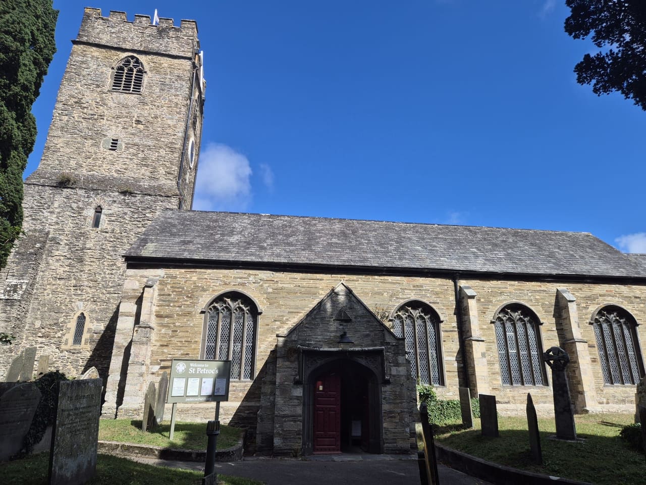 St Petroc's Church's tower rising against blue sky, with the nave's arched windows along its length